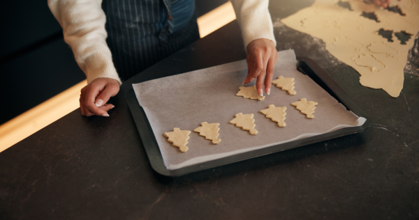 Žena peče vánoční cukroví ve tvaru stromečků